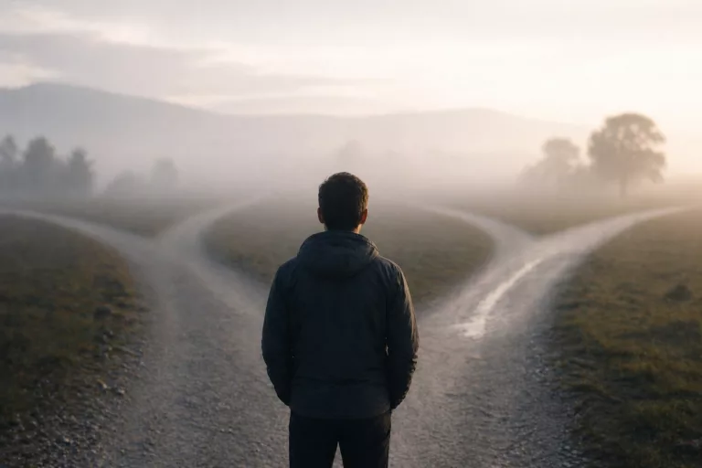 Eine Person steht an einer Weggabelung und schaut auf zwei verschiedene Wege.