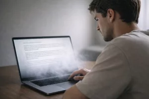 Junger Mann sitzt verärgert vor dampfendem Laptop KI Texte Marketing KI Texte im Marketing: Deshalb wirken sie nicht Textagentur Textineers